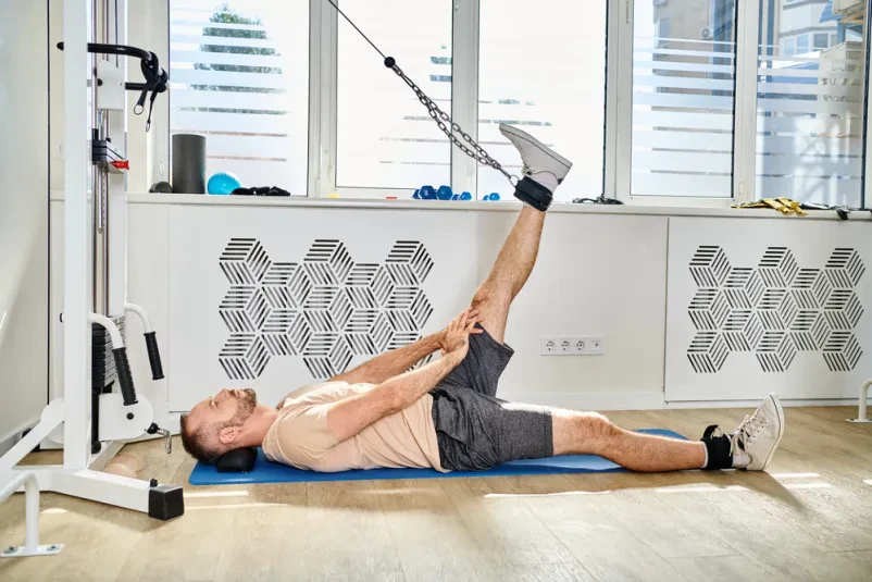 Moška vadba na moderni fitnes napravi v centru Moški na podlogi v kineziološkem centru izvaja vaje na fitnes napravi. To je Kvalitetna kineziološka vadba Ljubljana, okolica, ki pomaga pri moči.