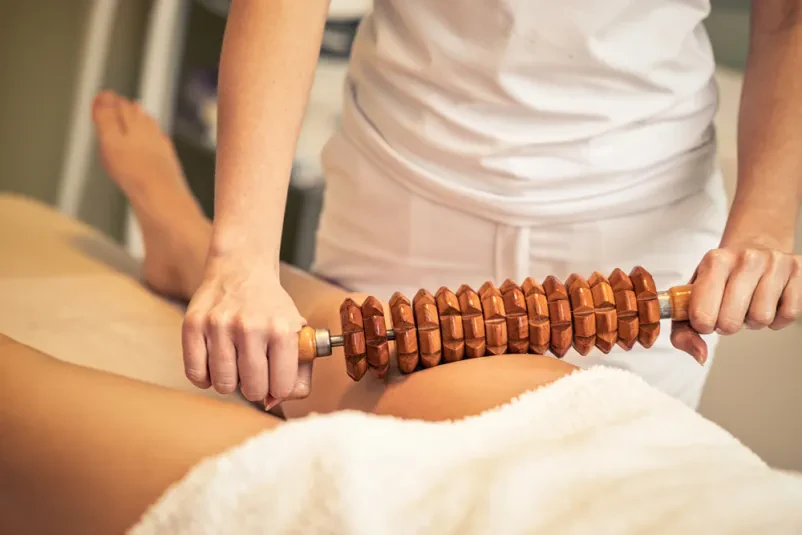 Maderoterapija za zmanjšanje celulita na nogi Terapevtka izvaja anticelulitno maderoterapijo na ženski nogi v spa salonu. Kvalitetna maderoterapija v Novem mestu izboljšuje prekrvavitev in gladi kožo.