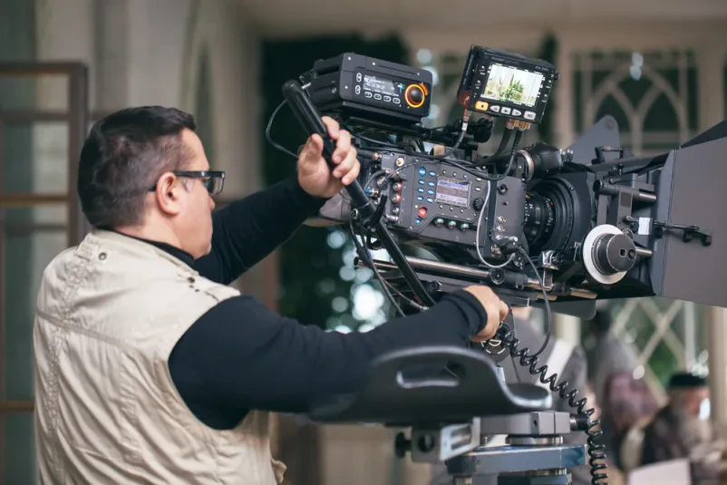 Izkušen snemalec z moderno profesionalno opremo med snemanjem filma. Njegova natančnost je ključna za zajem vsakega detajla.