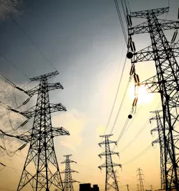 Impresiven daljnovodni stolp proti nebu med sončnim zahodom, ki simbolizira moč in prenos električne energije.
