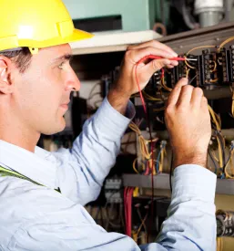 Električar v zaščitni čeladi preizkuša industrijski stroj v obratu. Nujno za optimalno delovanje montaže proizvodnih linij.