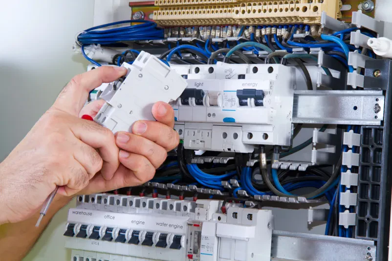 Moški električar skrbno sestavlja komponente v električnem panelu, kar je del osnovnih električnih inštalacij za dom.