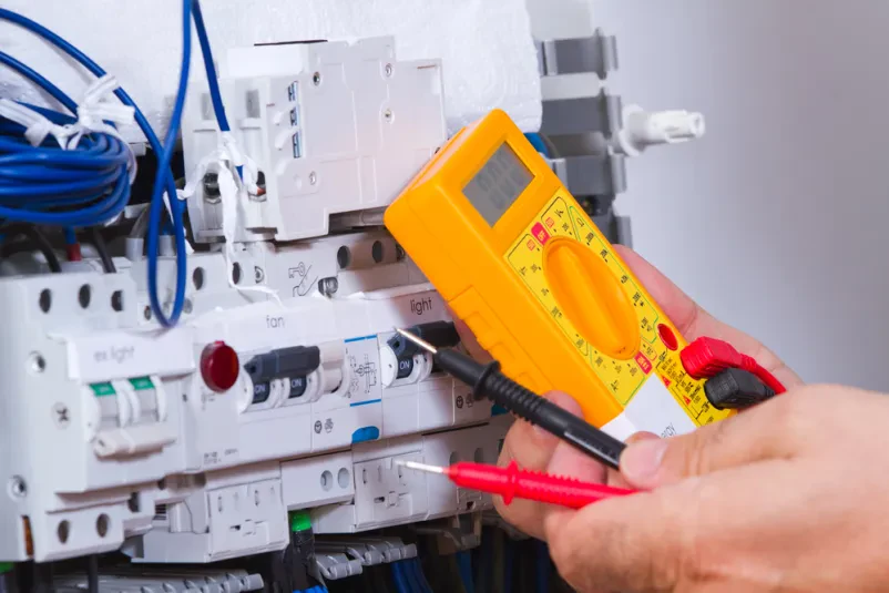 Podroben posnetek rok električarja, ki natančno priklaplja žice z izvijačem v električnem sistemu, poudarja preciznost dela.