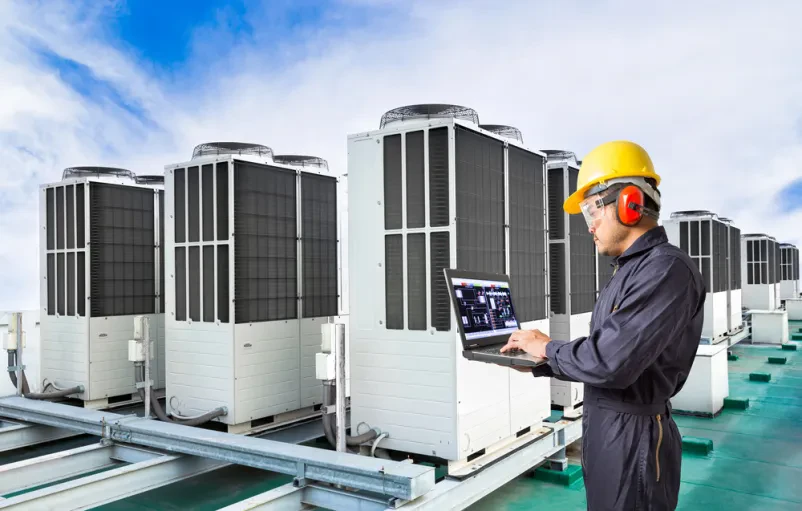 Inženir pregleduje klimatski sistem Inženir s prenosnim računalnikom pregleduje industrijski klimatski sistem na strehi tovarne, optimizira delovanje.