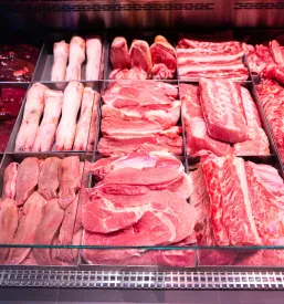 Različni kosi sveže svinjine, kot so vrat, jetra in jeziki, so pregledno predstavljeni v hladilni vitrini supermarketa.