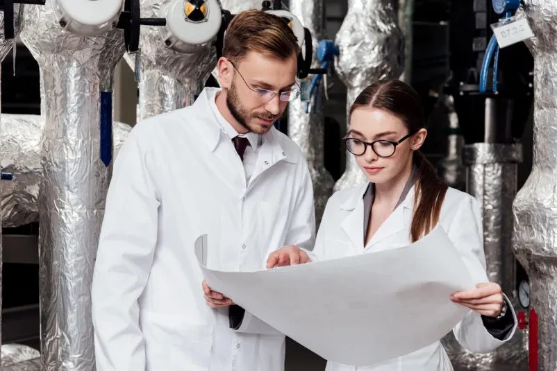 Inženirja pregledujeta načrt industrijskega sistema Dva inženirja v očalih se osredotočata na podroben načrt, ki prikazuje zasnovo industrijskega sistema kompresorjev, kar je ključnega pomena za kvalitetno konstruiranje industrijskih strojev v podjetjih v Goriški regiji.
