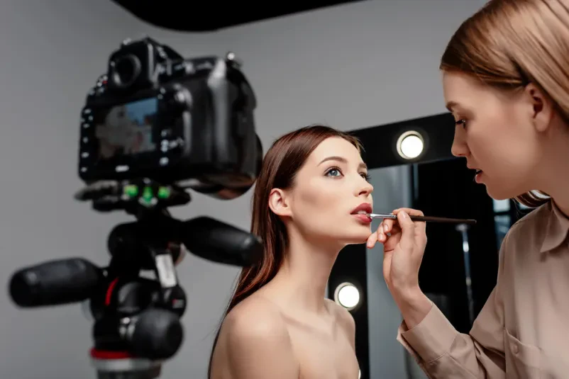 Profesionalna vizažistka nanaša sijaj za ustnice Umetnica ličenja previdno nanaša bleščilo na ustnice privlačnega modela, kar poudarja glamurozni videz in dopolnjuje celotno podobo.