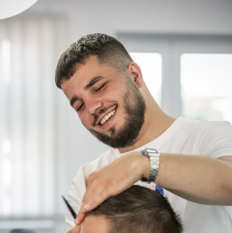 Stilsko striženje in urejanje brade v salonu Izkušen brivec skrbno striže in oblikuje pričesko stranki v modernem salonu, kar potrjuje, da je to najboljši frizer za moške v Mariboru.