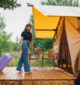 Popotnica z elegantno prtljago se sprehaja proti spalnici udobne glamping hiše, pripravljena na luksuzno bivanje in počitnice.