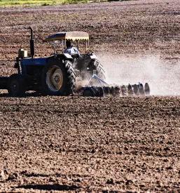 Velik traktor s kultivatorjem skrbno obdeluje zemljo in pripravlja gredice za pomladansko setev, kar je pomemben del kmetovanja, s katerim se spoznajo obiskovalci didaktične kmetije v Slovenskih goricah.