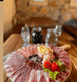 Skrbno narezan pršut, postrežen na leseni deski, ki čaka na goste. Odlična domača specialiteta za vsakogar.