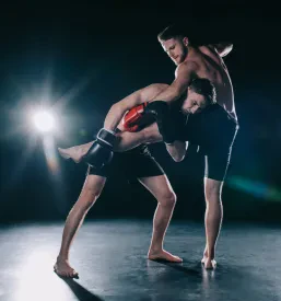 Dva bosa, mišičasta MMA borca v boksarskih rokavicah med klinčem in brco. Odličen primer za trening borilnih veščin in skupinske vadbe v Pomurju.