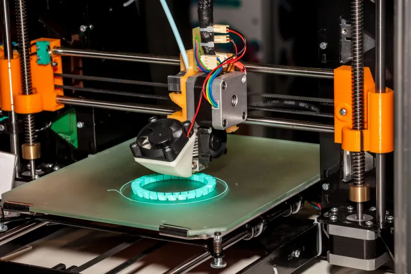 Od blizu posnetek delujočega 3D tiskalnika, ki z natančnostjo plast za plastjo gradi tridimenzionalni predmet iz materiala.