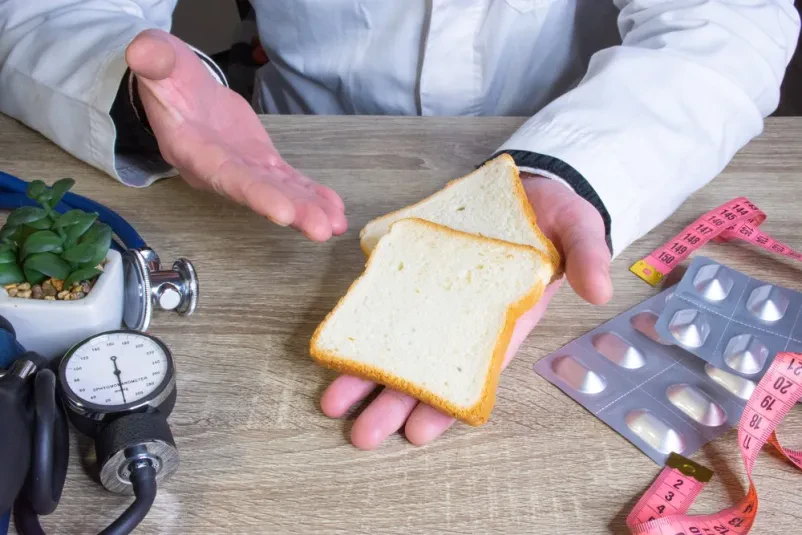 Nutricionist svetuje o pravilni uporabi kruha Zdravnik nutricionist med posvetom drži v roki in kaže pacientu kos kruha, pojasnjuje prehranske koristi in pomen v jedilniku.