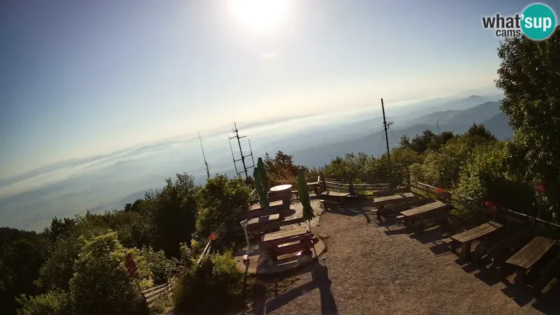 Širok panoramski pogled na naravno okolico in bližnje vrhove, ujet iz predela okoli planinske koče, ki prikazuje lepoto pokrajine.