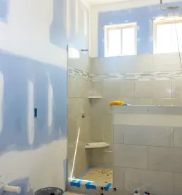 Pogled na nedokončano kopalnico med prenovo, z vidnimi instalacijami in pripravljenimi stenami za nadaljnje delo.