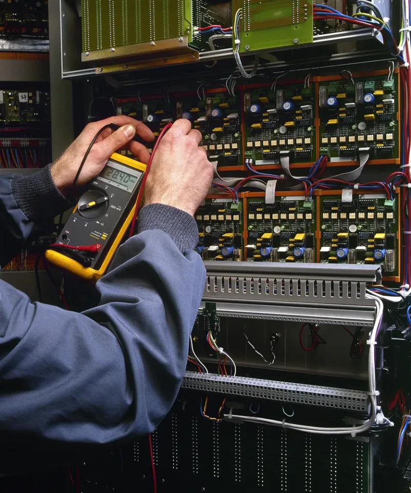 Električar pregleduje in testira industrijsko napravo. To je bistveni servis elektronskih strojev po Sloveniji za varnost in učinkovitost.
