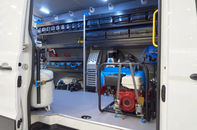 Podroben pogled v notranjost belega kombija, preurejenega v mobilno delavnico z urejenimi orodji in opremo za servis vozil.