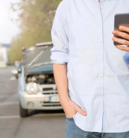 Moški ob cesti kliče mehanika na mobilni telefon, ko je njegovo vozilo obstalo zaradi okvare motorja, kar zahteva takojšnjo pomoč na terenu.