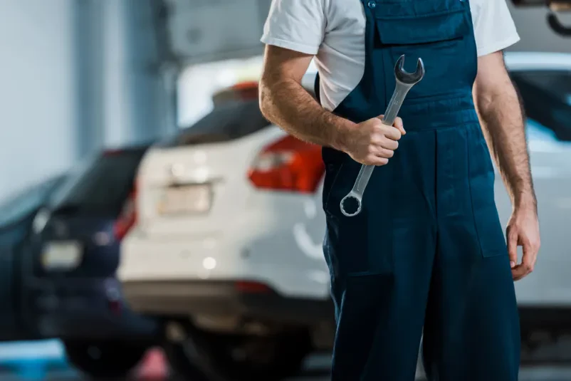 Mehanik drži viličasti ključ v avtoservisu Bližnji posnetek mehanika, ki drži velik viličasti ključ. Prikazuje pripravljenost na delo in natančnost pri avtoservisnih opravilih.