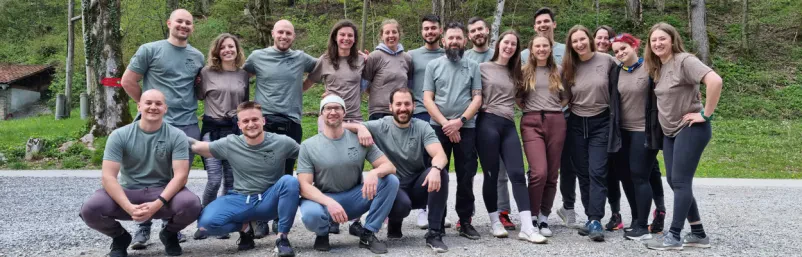 Skupinska delavnica v naravi Ljudje sedijo na travi in poslušajo predavatelja med delavnico osebne rasti, ki poteka v naravi na Dolenjskem.