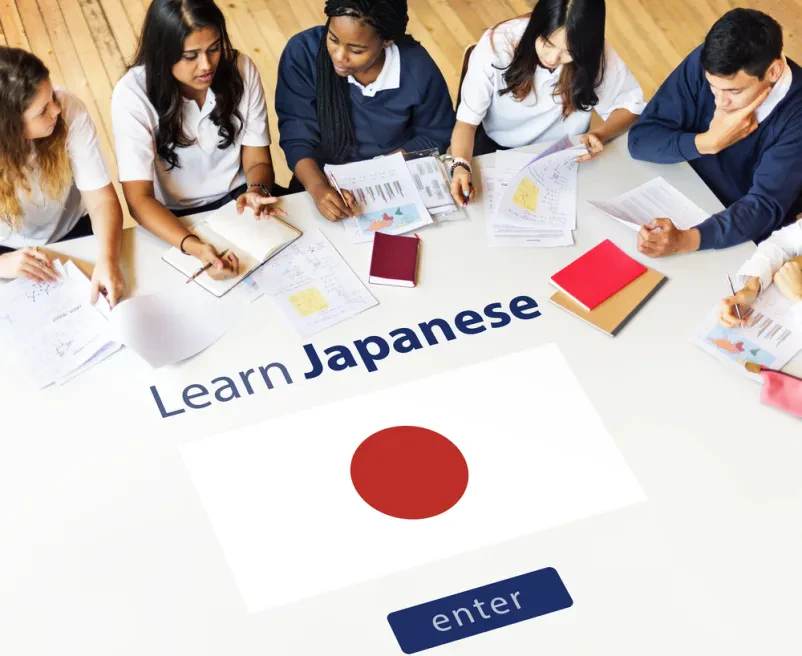 Skupina različnih študentov je zbrano osredotočena na učenje japonščine, zapisujejo si opombe na papirje, kar kaže na učinkovito poučevanje japonščine Bled, Gorenjska.