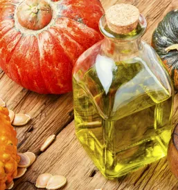 Steklenica bučnega olja in posoda z oljem, ob surovi buči. Odlična ponudba za prodajo bučnega olja Križevci, Ljutomer.