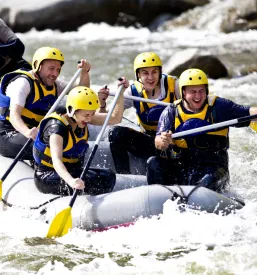 Vesela skupina ljudi v raftu z vodnikom uživa v adrenalinskem spustu po reki, idealnem za rafting na Muri Križevci.