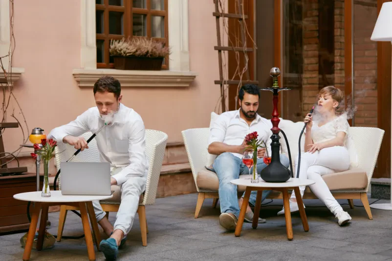 Sproščeno druženje s šišo in pijačo Par sproščeno kadi sadno šišo in pije v prijetnem lokalu. Shisha in kava bar Ljubljana Center je idealen za sprostitev ali delo na prenosniku.