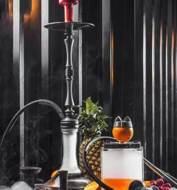 Elegantna, moderna šišo s steklenim podstavkom in kovinsko skledo, okrašena s svežimi kosi pomaranče in ananasa, oddaja dišeč dim.