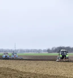 Detajl oranja njive, kjer traktor z močnim plugom obrača zemljo in jo pripravlja za spomladansko setev. Pomembno opravilo za kmetijsko pridelavo.
