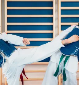 Dva otroka v belih taekwondo kimonih se s koncentracijo spopadeta v sparingu. Takšen trening tekwando Ljubljana Jarše gradi veščine.