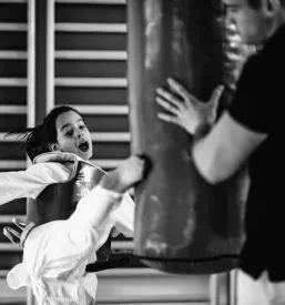 Mlada deklica z odločnostjo brca boksarsko vrečo med vadbo taekwondoja. Popolno za osebno trenerstvo in trening borilnih veščin v Murski Soboti, Pomurju.