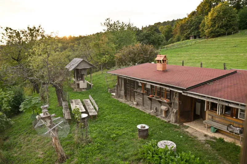 Ljudje in prijetno vzdušje pred glavno stavbo kmetije Družba ljudi uživa v sproščenem vzdušju pred tradicionalnim poslopjem naše turistične kmetije s sobami Sevnica, obdani z zelenjem.