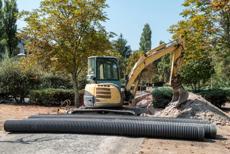 Mini bager med namestitvijo drenažnih cevi Mini hidravlični bager spretno namešča drenažne cevi velikega premera v sklopu projekta urbane infrastrukture, kar zagotavlja učinkovito odvodnjavanje.