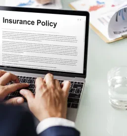 Poslovnež v pisarni uporablja prenosni računalnik, na zaslonu katerega je viden napis 'Insurance Policy'.