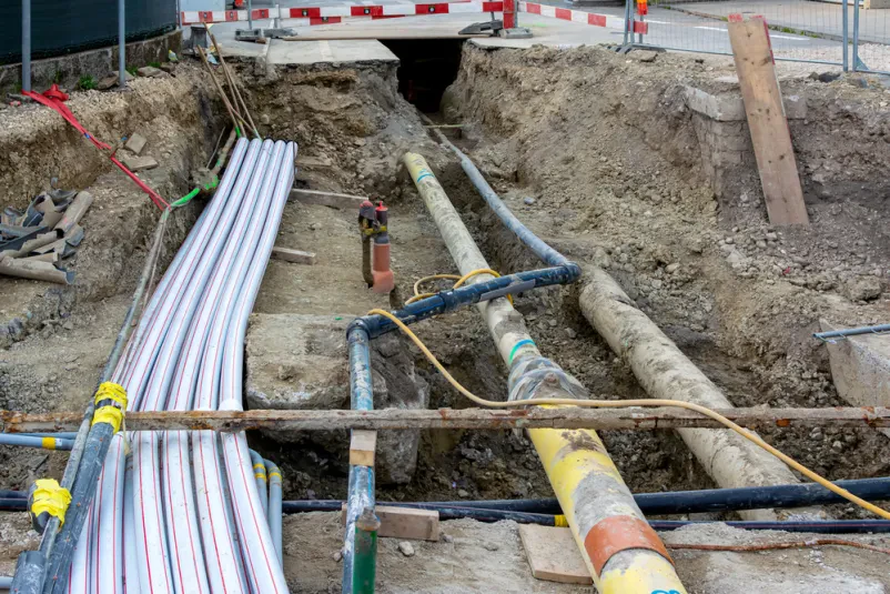 Položene komunalne cevi v jarku na gradbišču Različne komunalne cevi so skrbno položene v odprtem jarku na gradbišču, kjer potekajo obsežni izkopi za novo infrastrukturo.