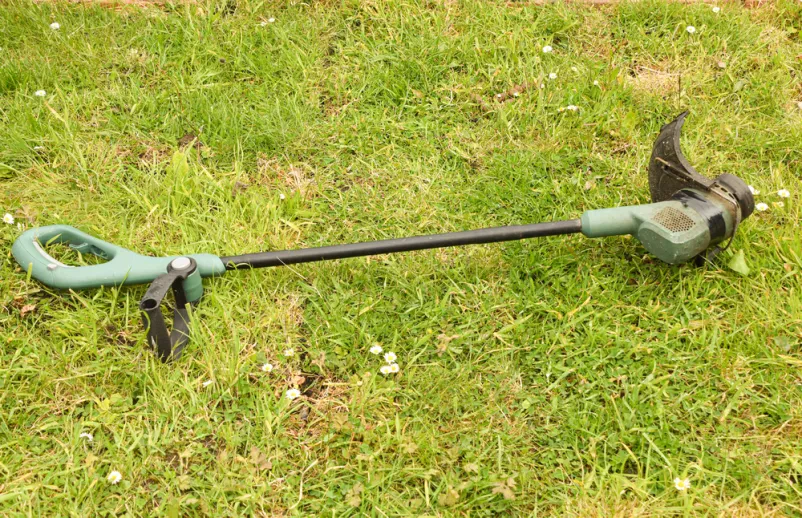 Natančno obrezovanje robov zelenice s trimerjem Vrtni trimer se uporablja za natančno obrezovanje robov trate v domačem vrtu, kar zagotavlja čisto in urejeno zeleno površino.