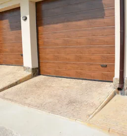 Moderna sekcijska garažna vrata v sivi barvi za dve vozili. Z urejenim dovozom tvorijo elegantno in funkcionalno rešitev za sodoben dom.