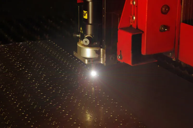 Laserski razrez jeklene pločevine z iskrami Laserski žarek natančno reže kovinsko pločevino v industrijskem obratu, ustvarjajoč intenzivne iskre. Ključen proces za učinkovito proizvodnjo.