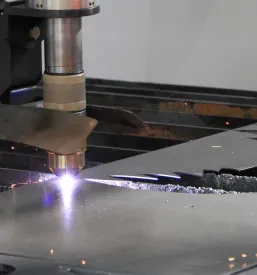 Laserski žarek precizno reže kovinsko pločevino v industrijskem okolju, kar zagotavlja visoko natančnost in avtomatizacijo v obdelavi kovin.