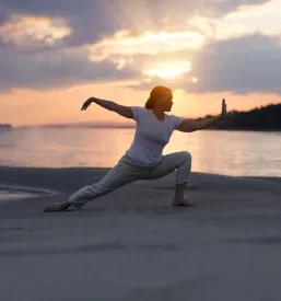 Ženska v sproščeni pozi vadi Tai Chi Chuan na peščeni plaži ob sončnem zahodu, ustvarjajoč mirno in osredotočeno vzdušje.