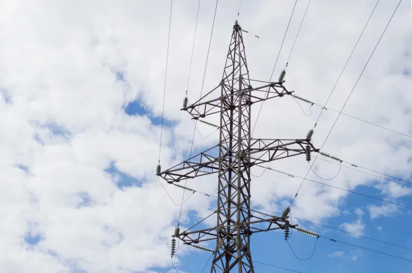 Stolpi visokonapetostnega daljnovoda pod modrim nebom Skupina mogočnih visokonapetostnih stebrov, ki prenašajo električno energijo, stoji pod širokim modrim nebom, predstavljajoč hrbtenico električnega omrežja.