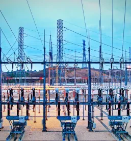 Kompleksna električna transformatorska postaja s številnimi žicami, izolatorji in opremo, ki zagotavlja distribucijo električne energije, posneta pred sončnim vzhodom.