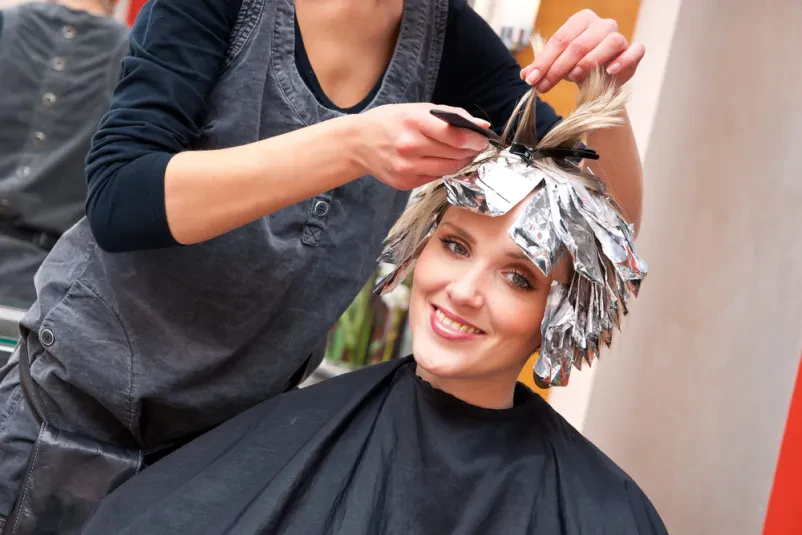 Barvanje las pri frizerju Bližnji posnetek ženske v frizerskem salonu med postopkom barvanja las, kjer frizerka skrbno nanaša barvo.