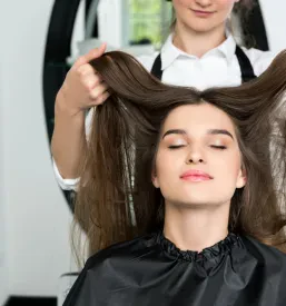 Srečna mlada ženska s sijočimi in lepo oblikovanimi lasmi v frizerskem salonu, zadovoljna z rezultatom. To je dober frizerski salon Železniki za žensko striženje.