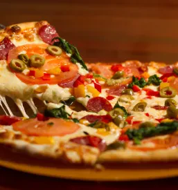 Približan posnetek sočnega kosa pice s topljenim sirom, pepperoni salamami in olivami, ki vabi k poskušanju. Odlična izbira za Dobra picerija Slovenska Bistrica, ki ponuja pice po naročilu.