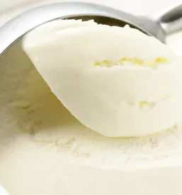 Gladka kepica kremnega vanilijevega sladoleda, postrežena v elegantni beli skodelici, obljublja osvežitev in užitek ob vsakem grižljaju.