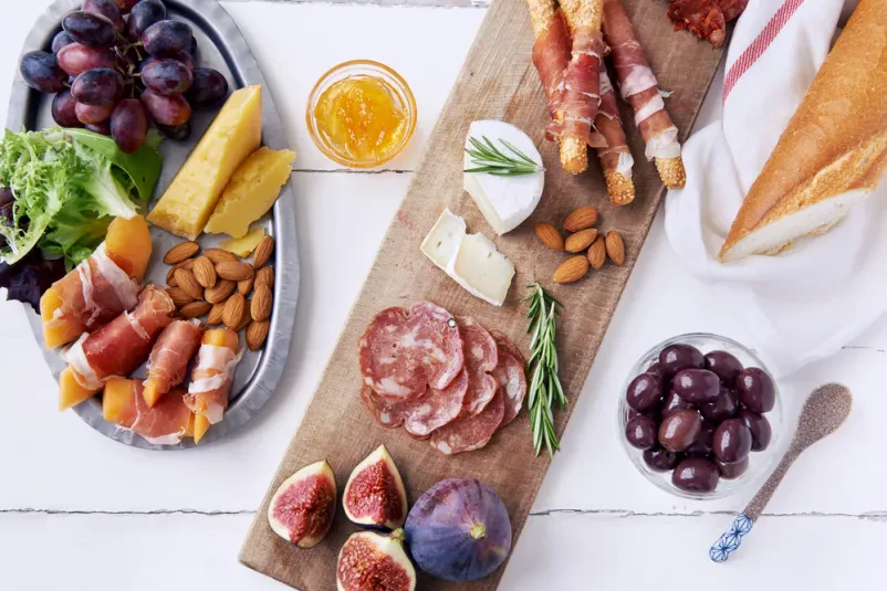Bogata mesna plošča z raznovrstnimi mesninami Pogled od zgoraj na bogato obloženo desko z domačimi suhomesnatimi izdelki Črnomelj, kot so salame, chorizo in pršut, skupaj s sirom in sadjem, za popolno pogostitev.