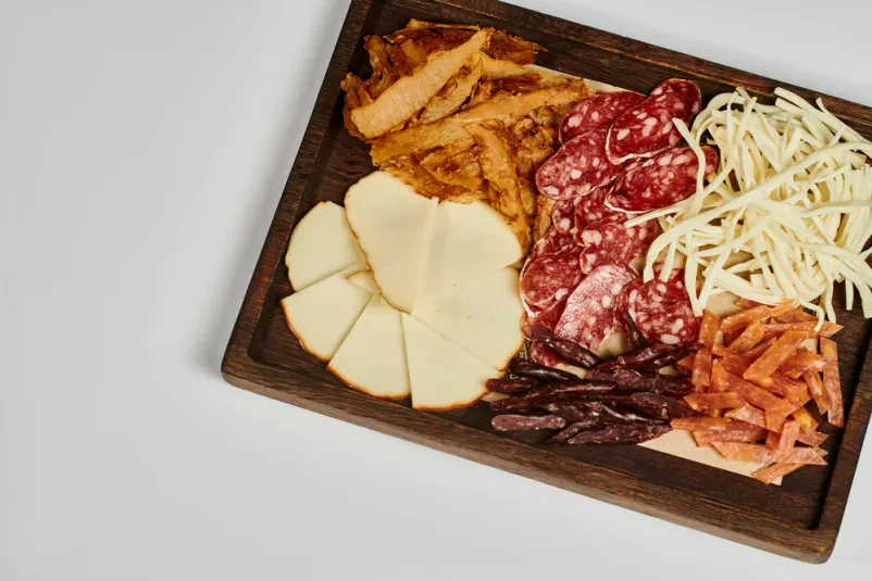 Plošča suhomesnatih izdelkov in izbranih sirov Eleganten servirni pladenj z razkošno izbiro domačih suhomesnatih izdelkov Črnomelj, vključno s sušeno govedino in rezinami salame, skupaj z gurmanskimi siri na sivi podlagi.